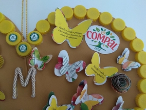foto 3 identifica os símbolos exigidos e a forma como foram utilizadas as embalagens para decorar o coração com flores e borboletas. E ainda a aplicação das frases e as tampinhas amarelas que contornam o coração.
