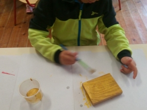 A criança pinta a base (bocado de madeira) em dourado.
