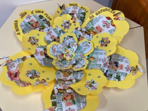 Flor e pétalas com embalagens Compal/Tetra Pak, alternadas com cartolina amarela e embalagens com o selo e símbolos visíveis Tetra Pak Protege o que é bom e Compal